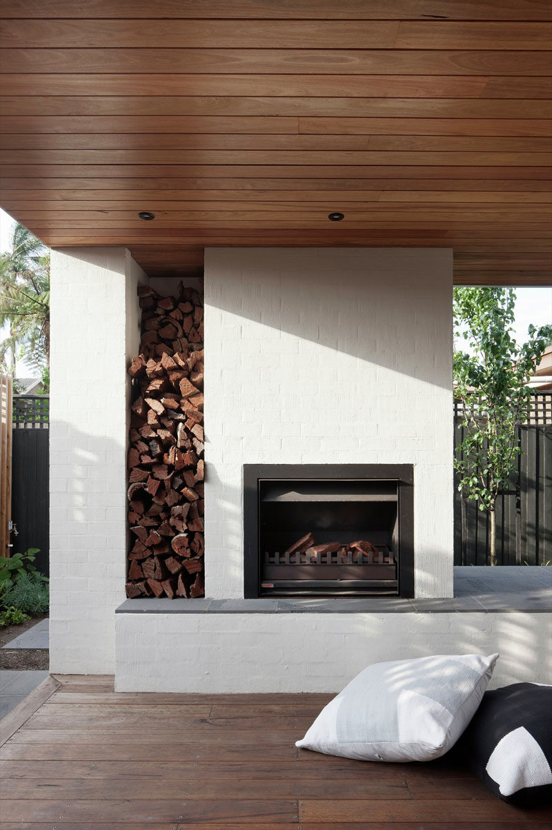 This outdoor fireplace is surrounded by brick that has been painted white. There's also a built-in space for firewood storage.