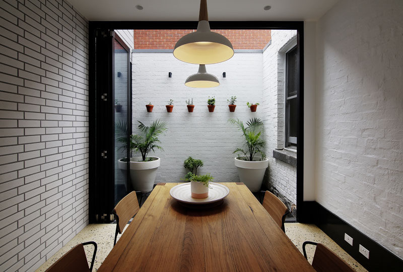 This dining room, surrounded by white bricks, opens up to a small private courtyard with wall-mounted plants.