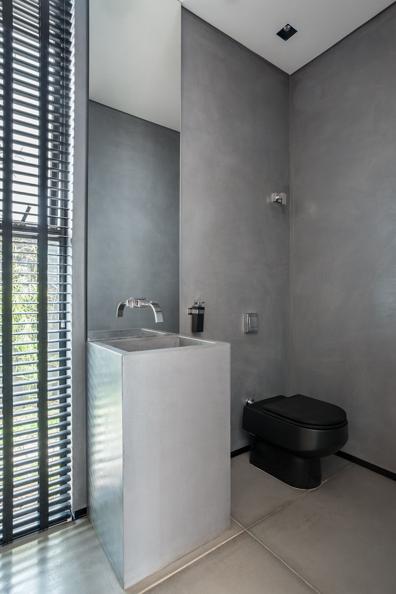 In this bathroom, there's a more masculine look with concrete walls and sink, a thin vertical mirror, and black toilet and shutters.