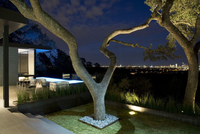 The fully landscaped yard of this house uses light to highlight the established trees and the low walls that surround the yard.