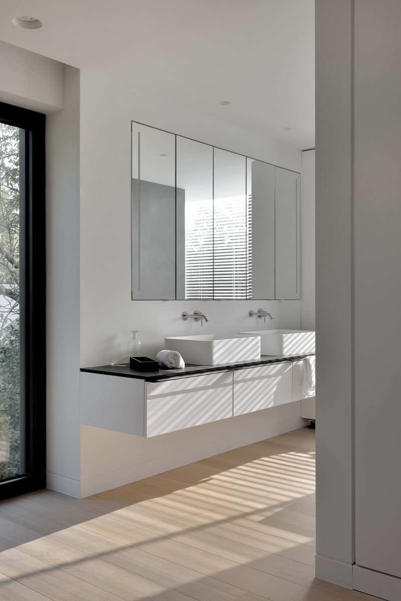 In this bathroom, large mirrors sit above the dual sink vanity and wooden floors help the space feel warm.