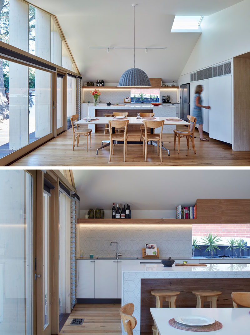 Inside the extension of this Australian home, the pitched ceiling and white walls make the space appear bright and large. At one end is the kitchen and the dining room.