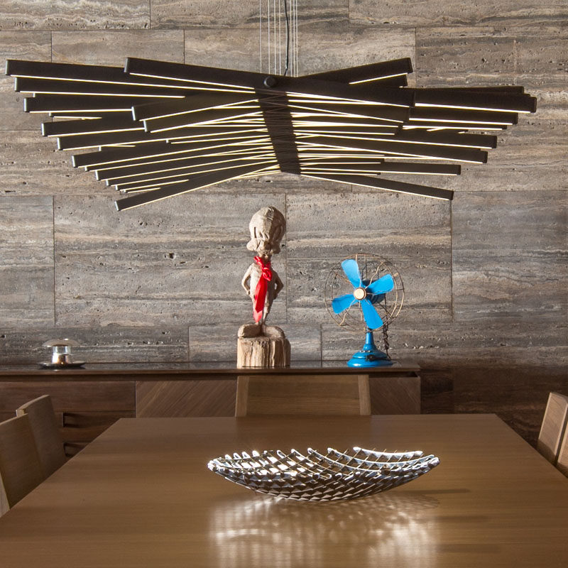 A sculptural light hangs directly above this dining table, while a wall of silver grey travertine runs the length of the home. #Lighting #DiningRoom