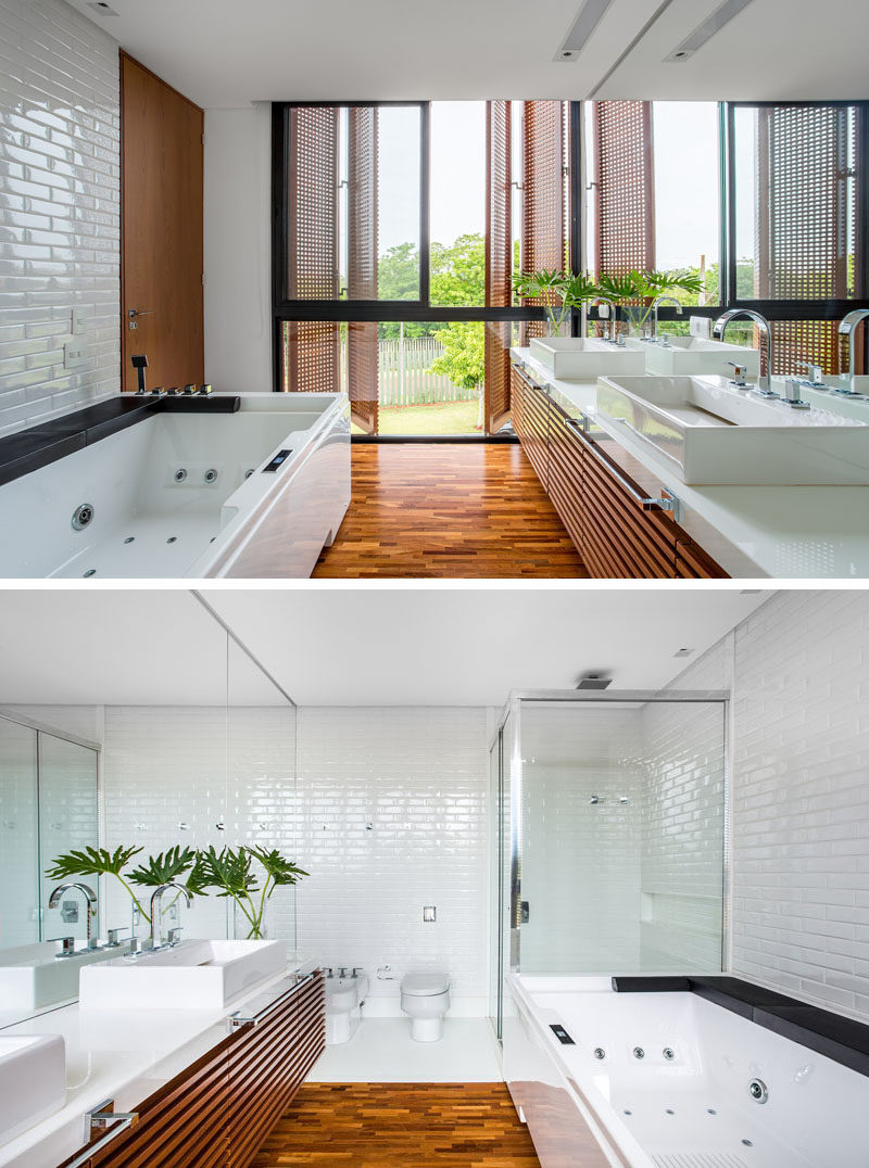 This bathroom has a wood and white palette with wooden floors, door, cabinetry and shutters, while the tiles, sinks, countertop and bath have been kept white.