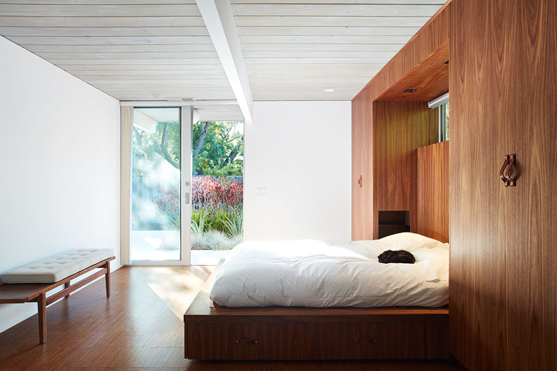 In this remodeled master bedroom, the bed now sits on a platform that's tucked within a wall of built-in wooden wardrobes with leather handles. By replacing the master closet with these built-ins the designers were able to create a large master bedroom.