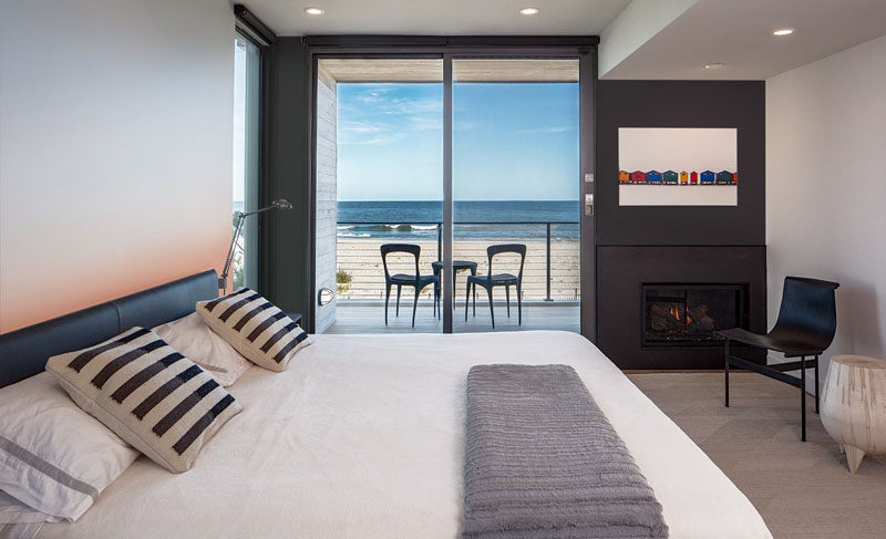 This bedroom in a modern beach house has a private balcony and a fireplace.