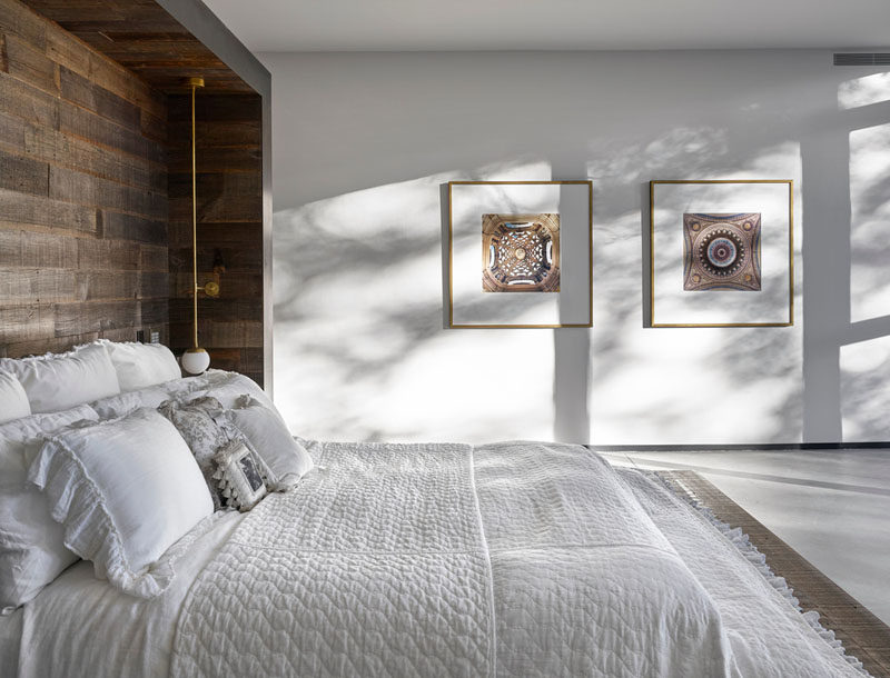 This master bedroom has a wooden feature wall and looks out towards the backyard with large windows providing framed views of the treetops. 