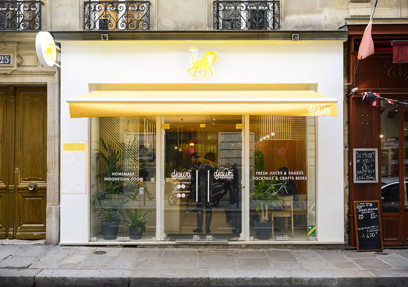 The exterior of this contemporary restaurant is bright white with yellow accents, and large windows and glass doors allow people walking by to easily see into the restaurant.