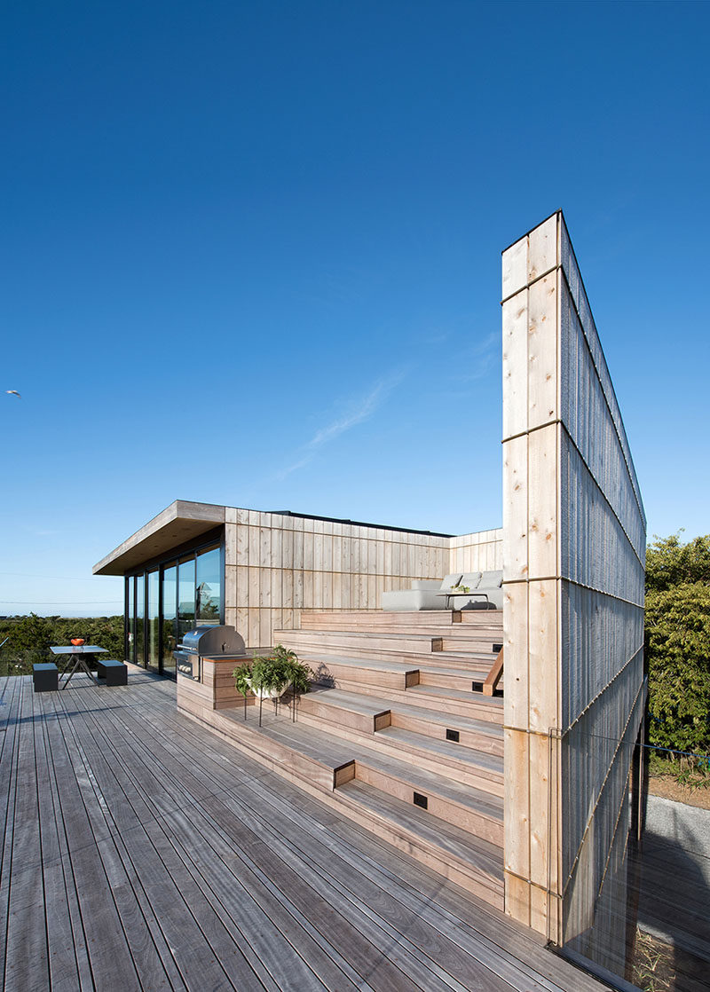 The outdoor space on the upper level of this home has an outdoor dining area, a built-in bbq and a tiered wooden seating area that's sheltered from the wind.