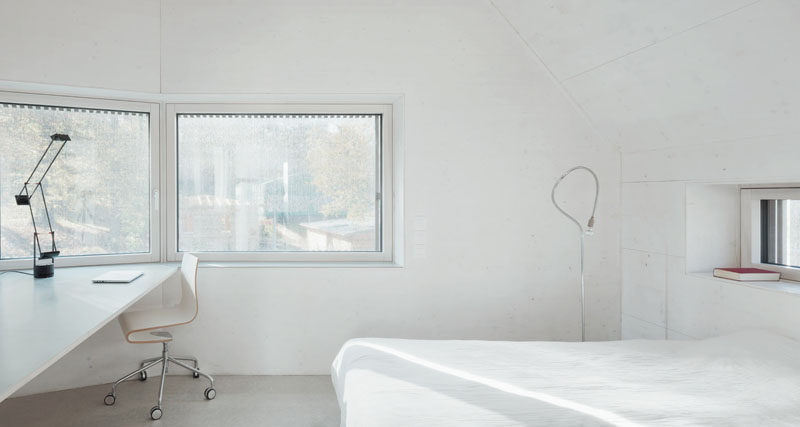 In this white bedroom there's a built-in desk, lots of windows and a light grey concrete floor.