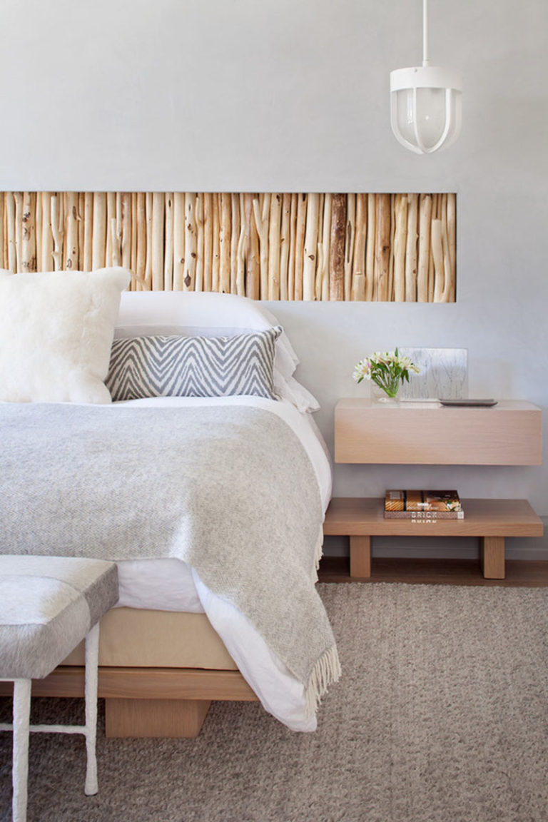 A recessed wall section filled with rustic branches acts as a headboard above this bed