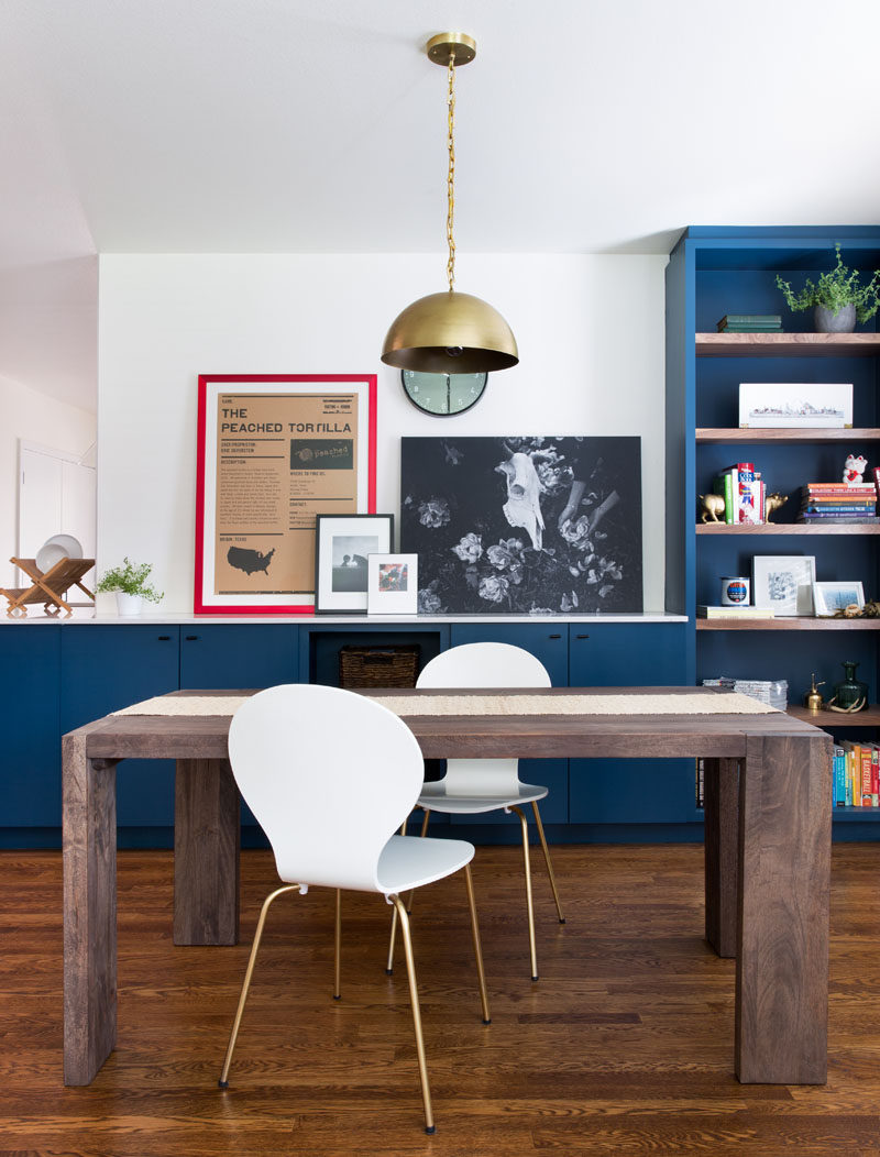 This Home In Austin Received An Updated White And Navy Blue Kitchen // The navy blue cabinetry, black hardware and brass accents create a simple yet sophisticated look in the kitchen while pops of color, like the red frame and colorful book on the shelf, bring in a touch of excitement and fun.