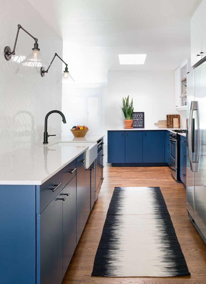 This Home In Austin Received An Updated White And Navy Blue Kitchen // Simple white tile arranged in a herringbone pattern covers the wall behind the sink and makes up the backsplash around the rest of the kitchen. It creates a contrast against the dark hardware and navy cabinets to make the space look clean and contemporary.