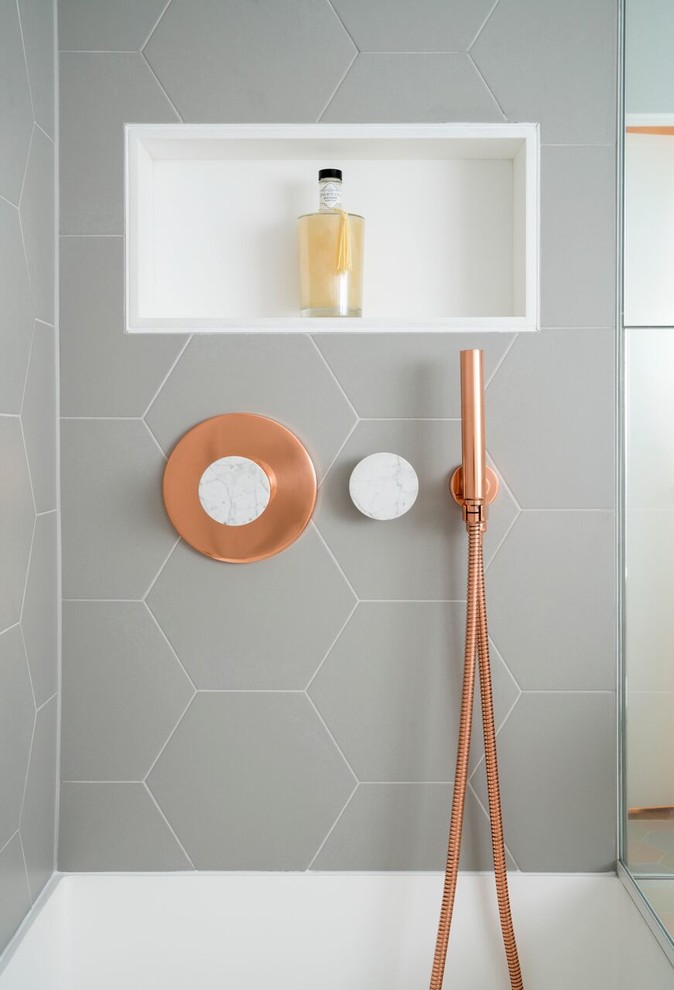 This bathroom features copper and marble fixtures next to light gray hexagon tiles