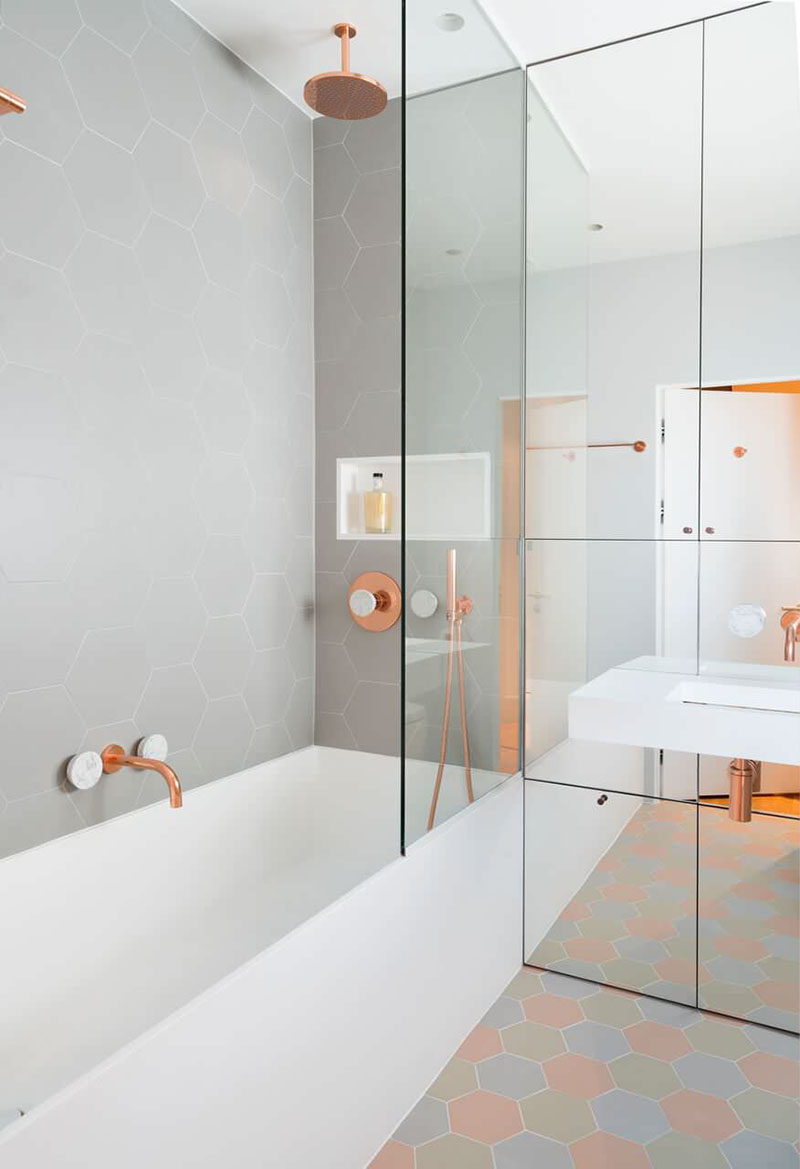 This bathroom features copper and marble fixtures next to light gray hexagon tiles