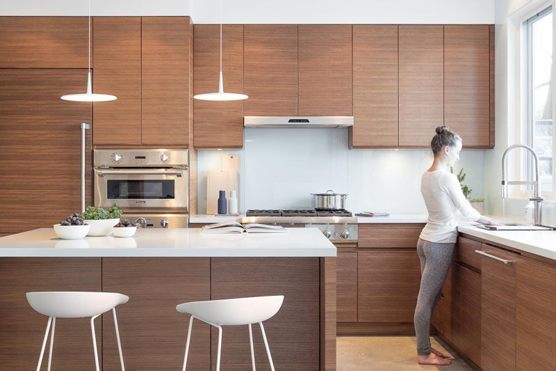 Walnut kitchen cabinets and white quartz countertops with a glass backsplash make up the color palette in this modern kitchen.