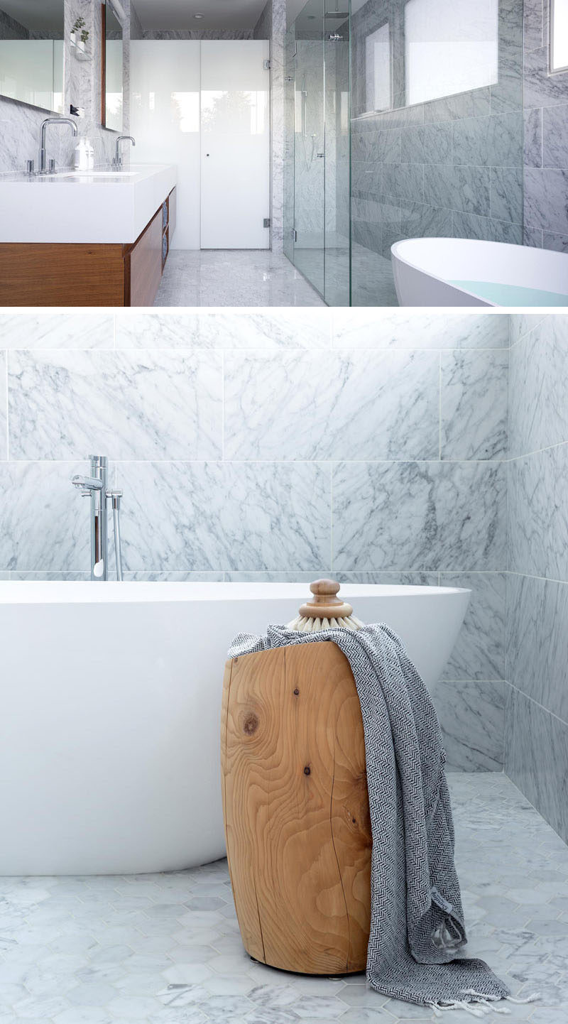 This modern bathroom has white Carrara marble for the floors and walls, a glass shower surround, a white quartz countertop and a walnut vanity.