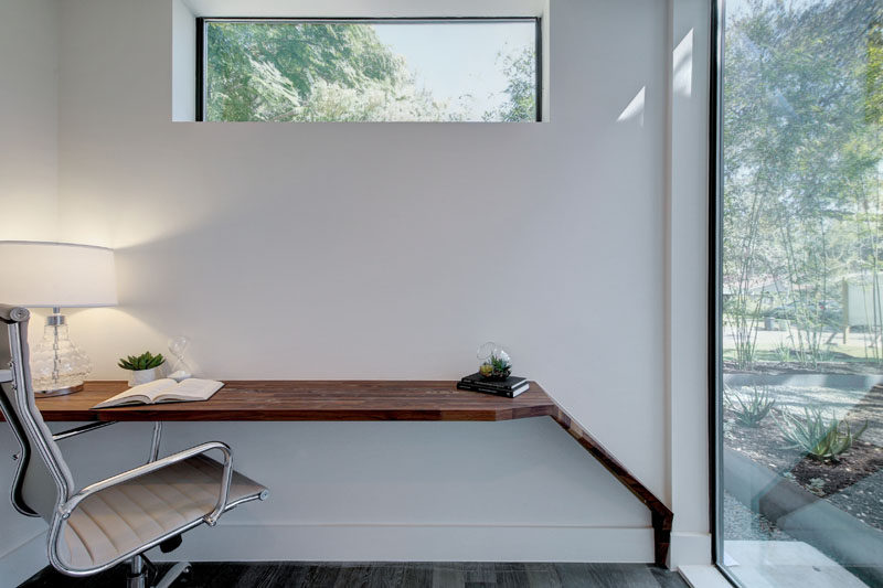 This small home office with a built-in wood desk has views of the garden through a large floor-to-ceiling window.