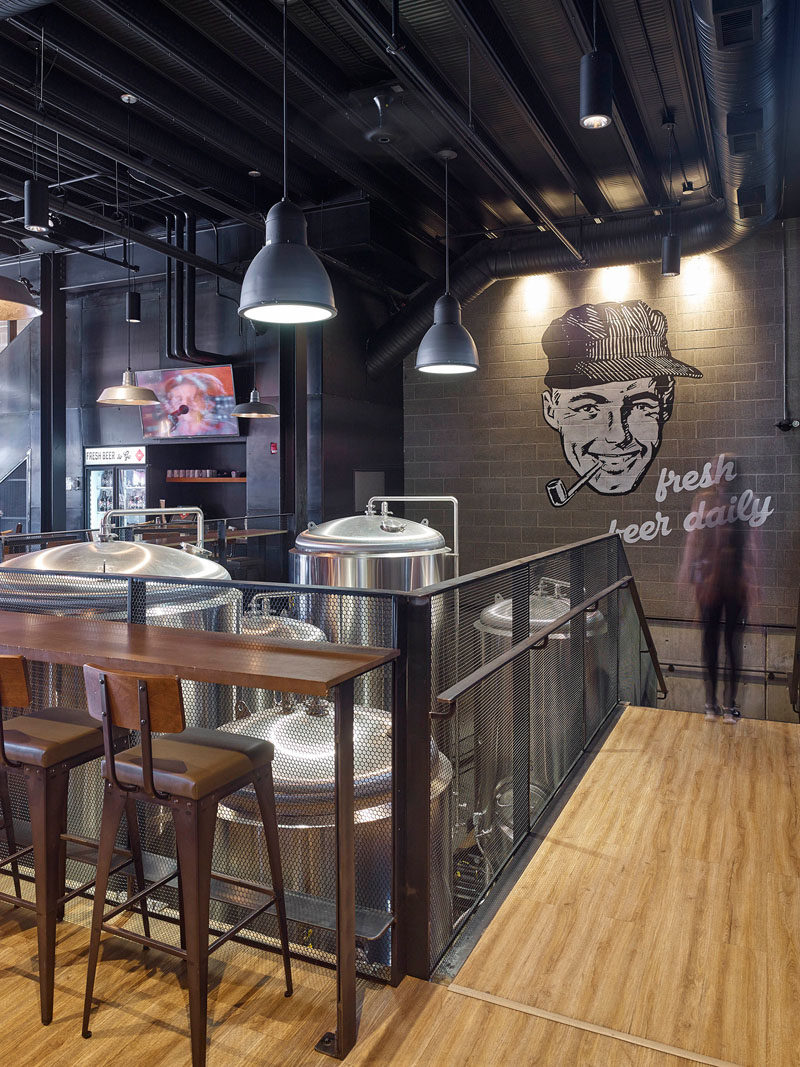 This industrial inspired brew pub and restaurant design features a large wall mural and glimpses of the beer making equipment.