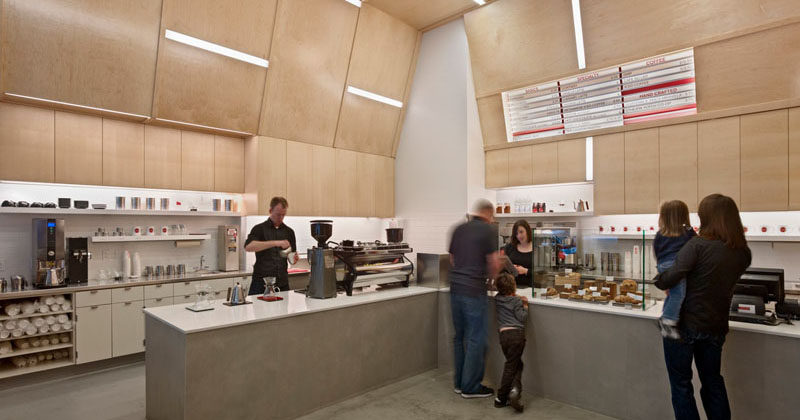 This modern coffee shop design has the walls and ceiling covered in plywood. Embedded within the plywood walls are strips of lighting creating a unique and artistic design.