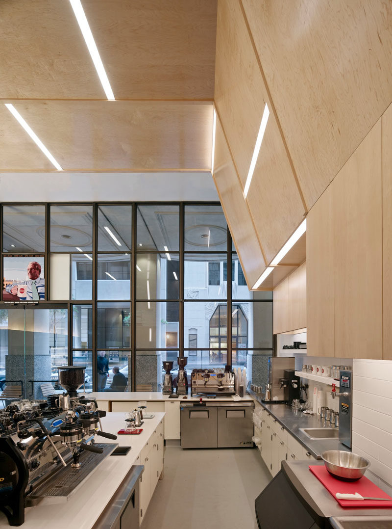 This modern coffee shop design has the walls and ceiling covered in plywood. Embedded within the plywood walls are strips of lighting creating a unique and artistic design.