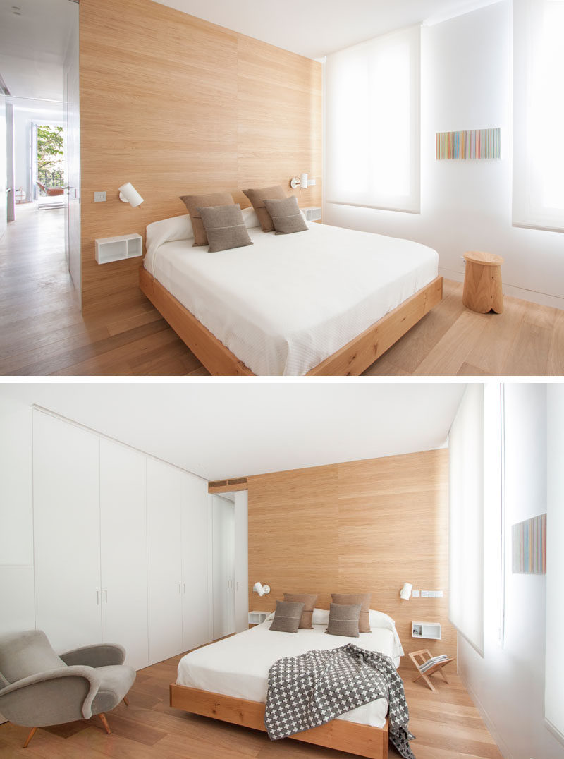 In this modern bedroom, white walls and window shades are broken up by light wood details, like the floor, accent wall and bed frame. Opposite the windows is a wall of white cabinetry that almost blends in to the surrounding wall.