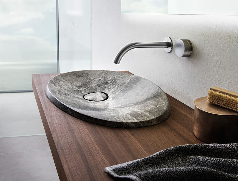 This modern bathroom sink made from natural stone sits on a floating wood vanity and has a simple stainless steel faucet.