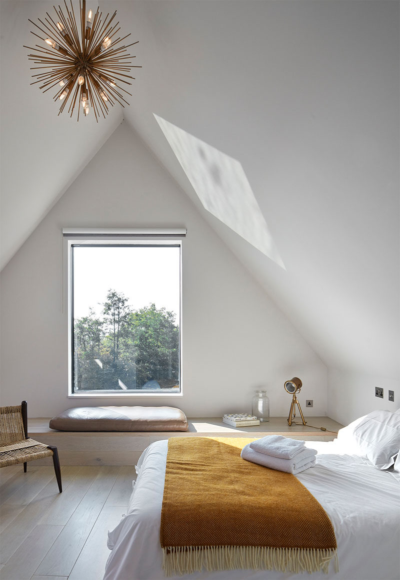 This white modern bedroom has a small window that can be enjoyed when sitting on the built-in bench seating.