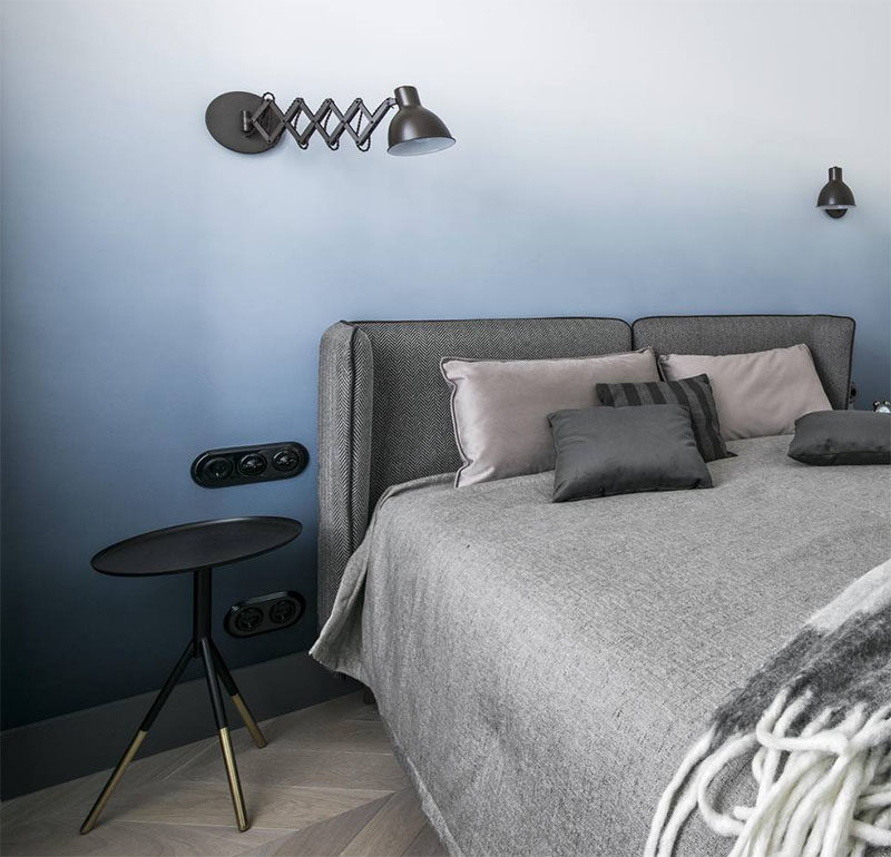 This modern bedroom has a soft blue ombre accent wall behind the grey upholstered bed.