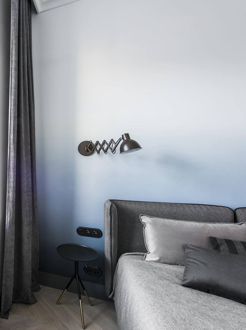 This modern bedroom design features a soft blue ombre accent wall, and grey bedding and curtains.