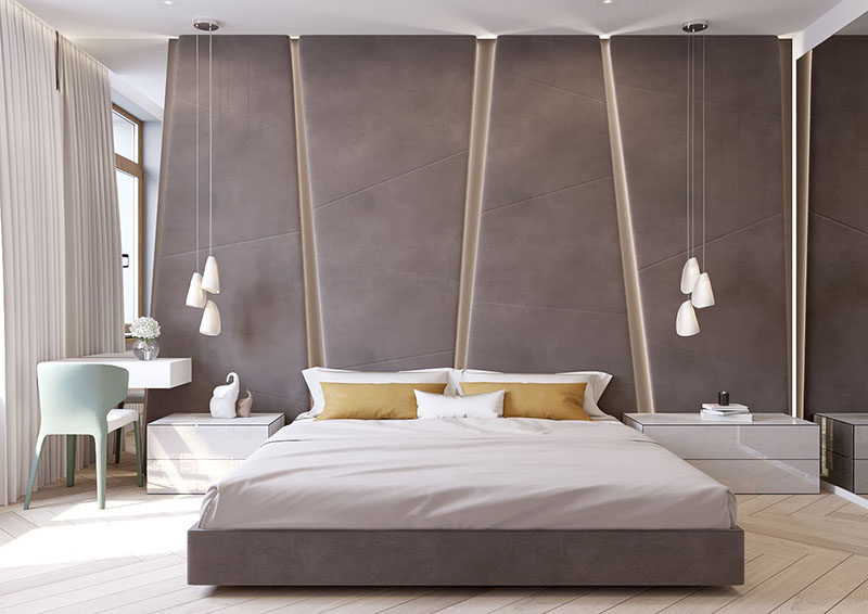 The grey upholstered headboard in this modern bedroom almost takes up the entire wall. The angular panels have hidden lighting between them giving the bedroom a soft glow.