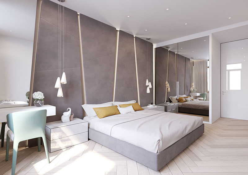 The grey upholstered headboard in this modern bedroom almost takes up the entire wall. The angular panels have hidden lighting between them giving the bedroom a soft glow.