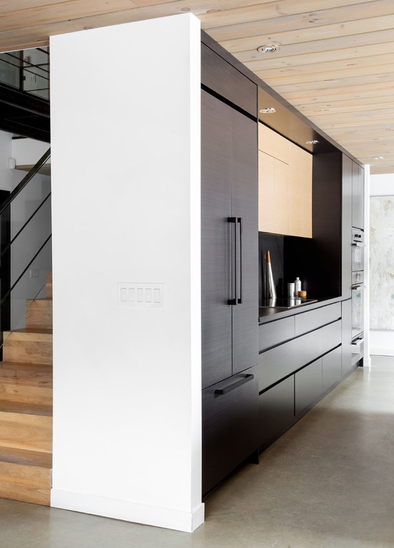 This modern black kitchen features an integrated fridge and freezer, an integrated stove top and an island to make preparing meals easy and convenient.