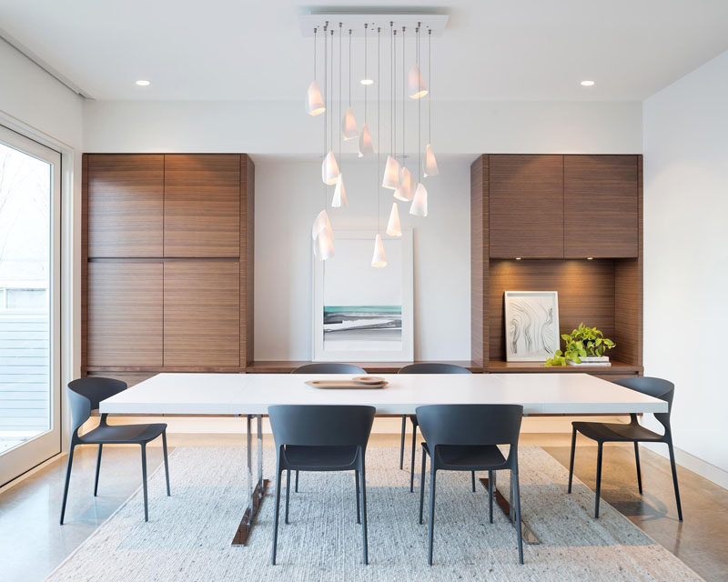 In this modern dining room, sculptural pendant lights hang from the ceiling, while built-in walnut cabinets create plenty of storage space.