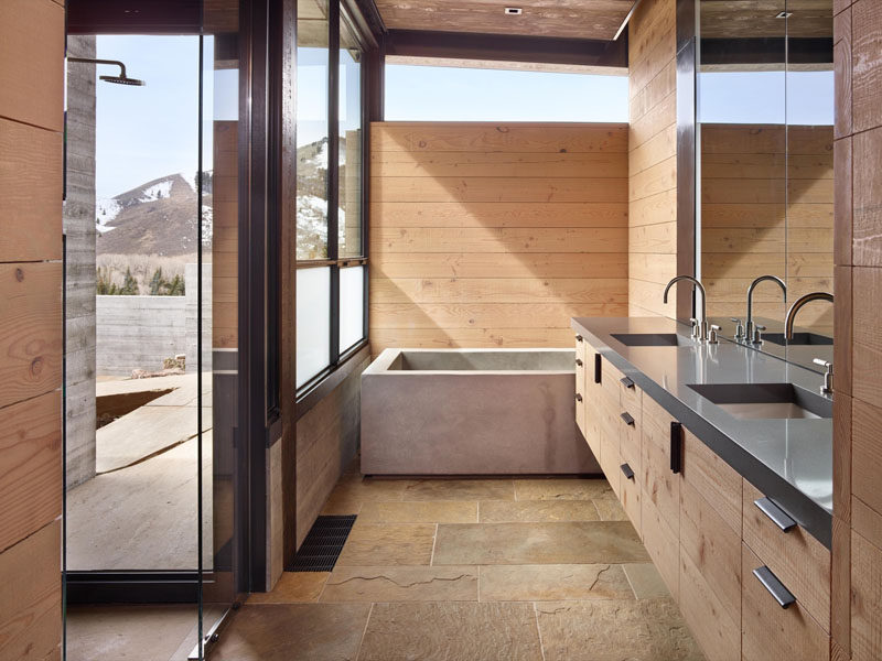 In this industrial modern bathroom, wood and stone tiles have been paired with a concrete bathtub. In the shower, there's a floor-to-ceiling window so that you can have mountain views while relaxing.