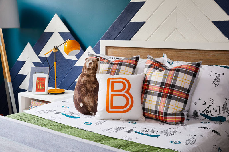 This kids bedroom design includes includes elements from the great outdoors, like a mountain range with hidden lighting that mimics the colors of the Northern Lights, camping inspired sheets, and a grizzly bear throw pillow.