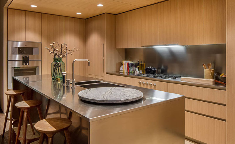 This modern kitchen features honey-hued American oak cabinets with satin-finish stainless steel countertops and backsplashes. Dornbracht faucets have been used for the sink, and for the floor, light colored quartz has been used in the kitchen, while oil finished oak flooring has been used in the rest of the apartment.