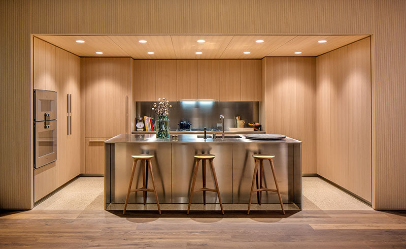 This modern kitchen features honey-hued American oak cabinets with satin-finish stainless steel countertops and backsplashes. Dornbracht faucets have been used for the sink, and for the floor, light colored quartz has been used in the kitchen, while oil finished oak flooring has been used in the rest of the apartment.