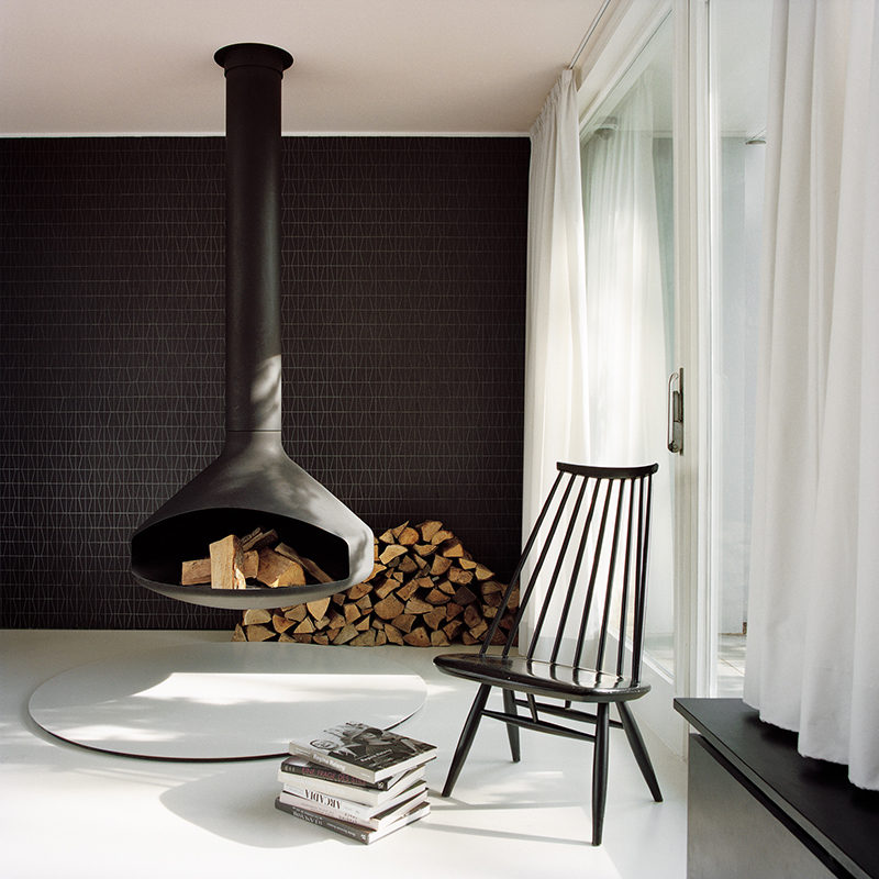 In this modern living room, a hanging fireplace matches the black tile accent wall and the several pieces of black furniture.