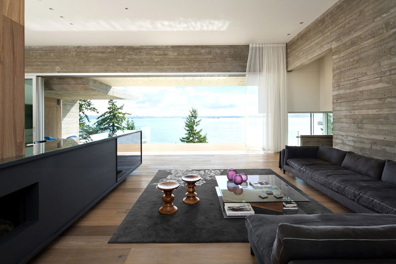 In this modern living room, a low profile sofa and dark rug define the area, while the television is is tucked into a cabinet. The living room also opens up to the deck outside.