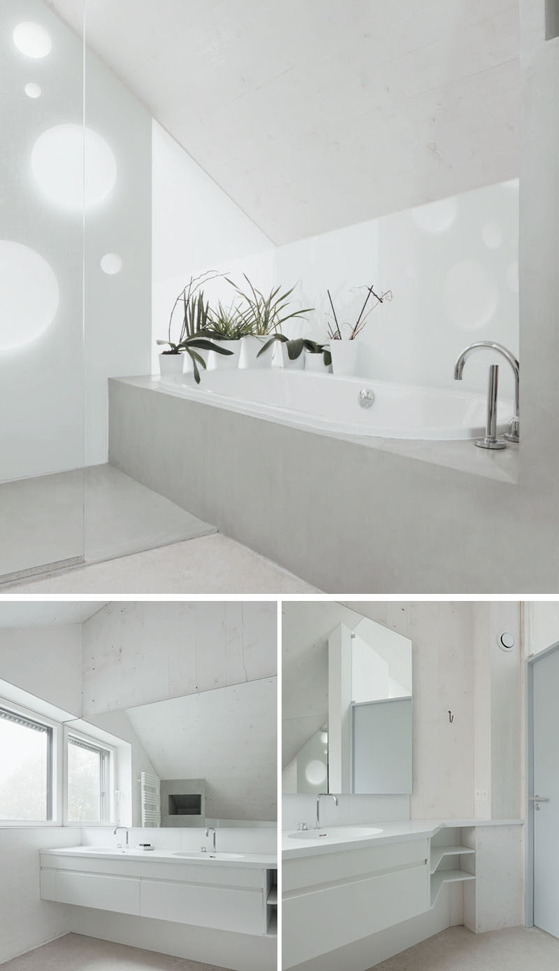 The white and light concrete bathroom in this modern home is simple in its design. There's a built-in bathtub, a glass enclosed shower and an angled vanity. 