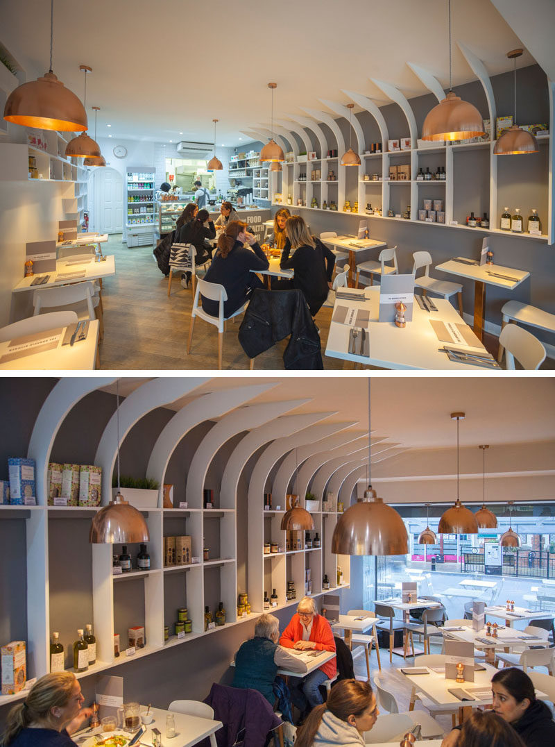 In this modern resturant interior, the designers used white for the walls, furniture, and shelves, wood on the floors and chair legs, copper accents in the form of pendant light fixtures, table stands, and salt and pepper shakers. A grey accent wall is used to draw your eye to the white shelves.