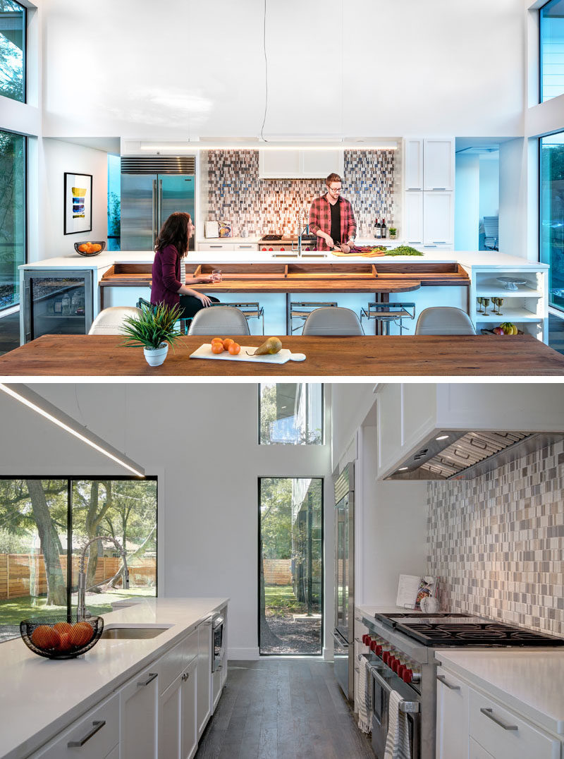 This modern kitchen has a large island with a built-in wood bar, and at one end there's a small drinks fridge, and at the other end is open shelving. White cabinets keep the space bright and patterned tiles used for the backsplash add an artistic touch.