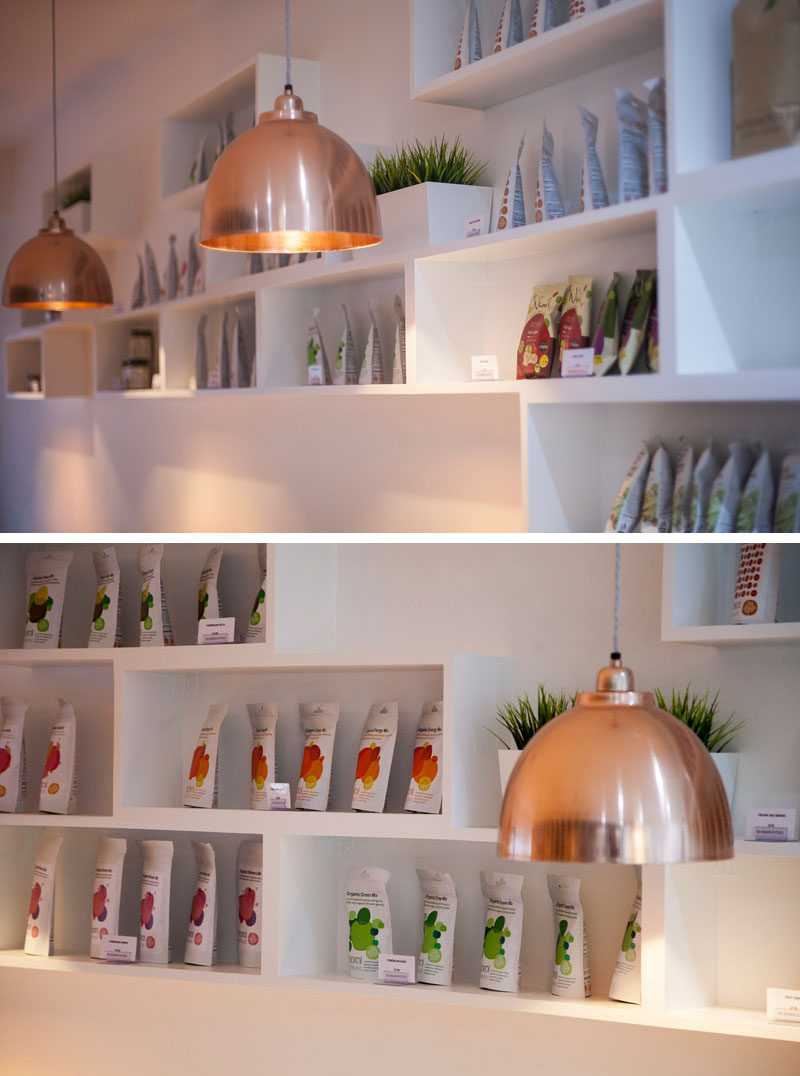 This modern restaurant interior features a copper pendant lights throughout, and a sculptural shelving unit displays the various products that they sell.