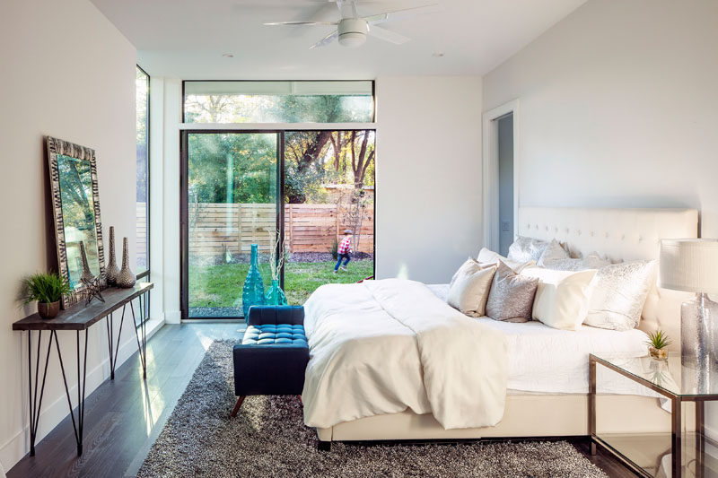 This master bedroom suite has access to the backyard, while wooden floors and a light brown rug have been paired with a cream colored bed and light walls.