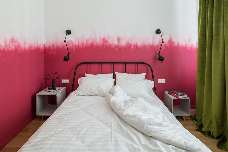 Oksana Dolgopiatova has designed a bedroom that features pink and white walls. While the lower part of the wall is solid pink, the top part of the pink blends into the white wall with visible vertical brush strokes creating an ombre effect.