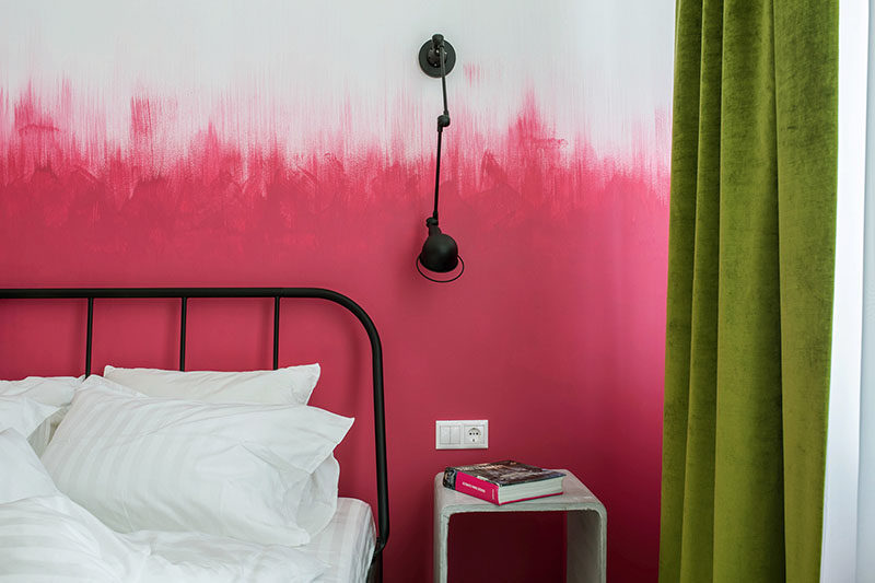 Oksana Dolgopiatova has designed a modern bedroom that features pink and white walls. While the lower part of the wall is solid pink, the top part of the pink blends into the white wall with visible vertical brush strokes creating an ombre effect.