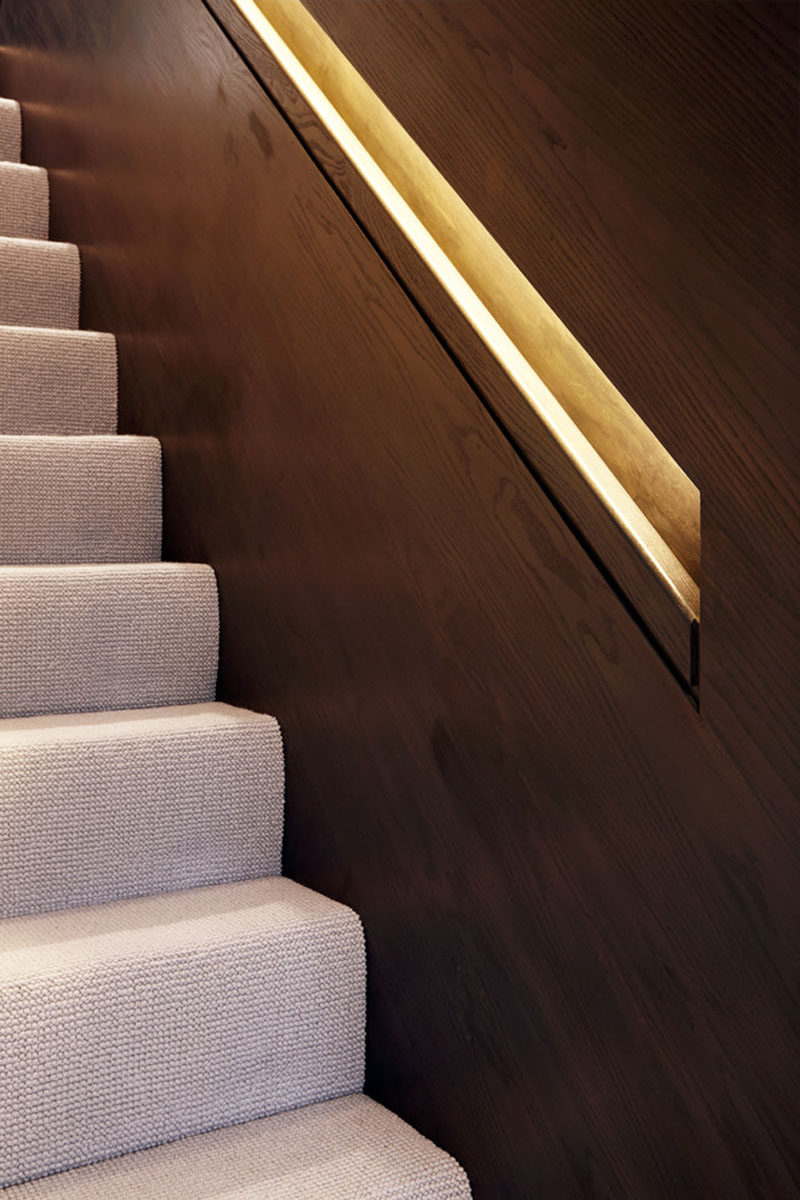 The lighting in the built-in handrails of these modern wooden stairs, is concealed by the top part of the railings and continues from the bottom of the staircase all the way up to the top floor.