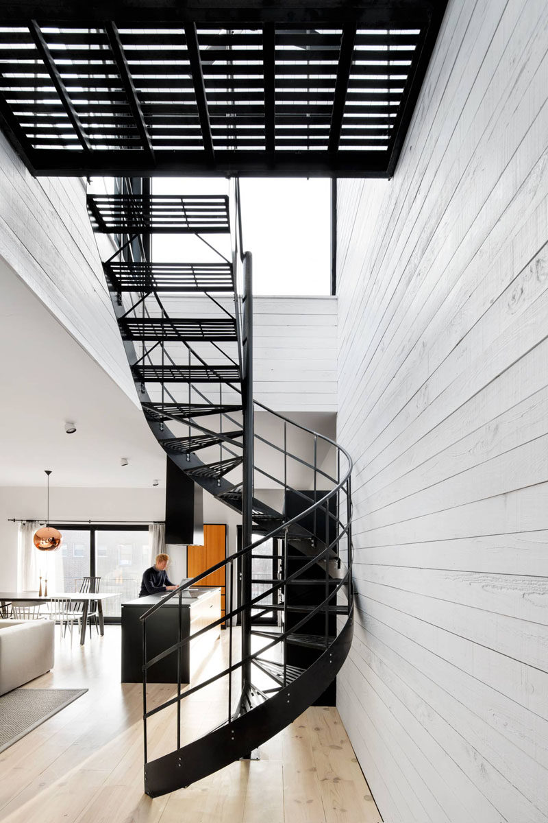 A simple matte black metal spiral staircase with grated steps connects the two main floors of this modern house and lets light easily pass through to keep the space feeling bright and airy. #SpiralStairs #SpiralStaircase #ModernSpiralStairs