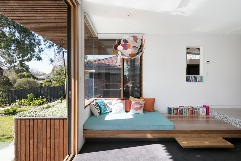 This modern house features a built-in daybed with a thick mattress on top, and it sits up against a wrap-around corner window to create a cozy reading spot lit up by both a colorful pendant light and the natural light coming through the windows.